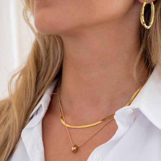 Close-up of a person wearing gold hoop earrings and necklaces against a white background