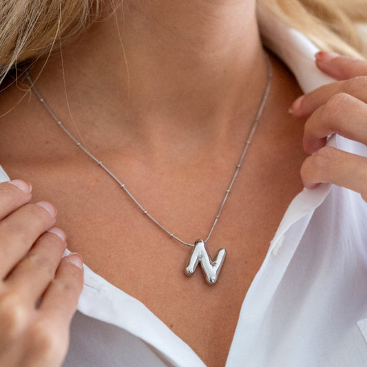 Close-up of a person wearing a silver necklace with a 'N' initial pendant.