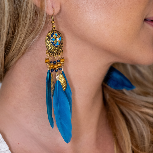 Close-up of a person wearing blue feather earrings with gold and blue accents.