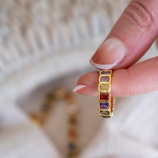 Gold ring with multicolored gemstones held by a hand, blurred background
