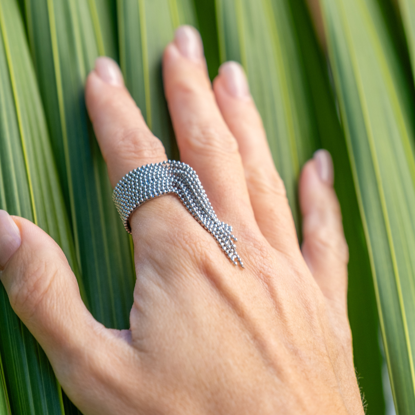 Hand wearing a silver ring against a green leaf background