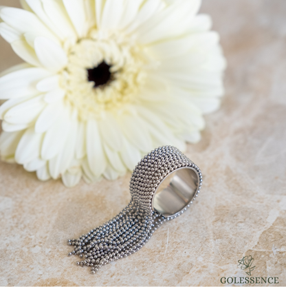 Silver ring with textured band and smooth surface next to a white flower on a beige background