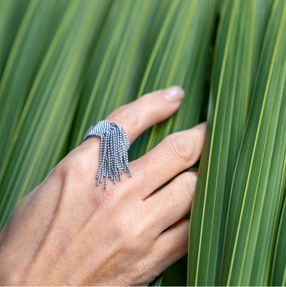 Hand wearing a textured ring on a palm leaf background