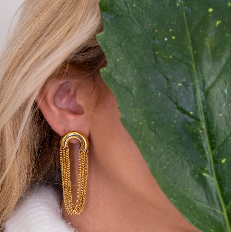 Gold tassel chain earring worn by a person with a leafy background