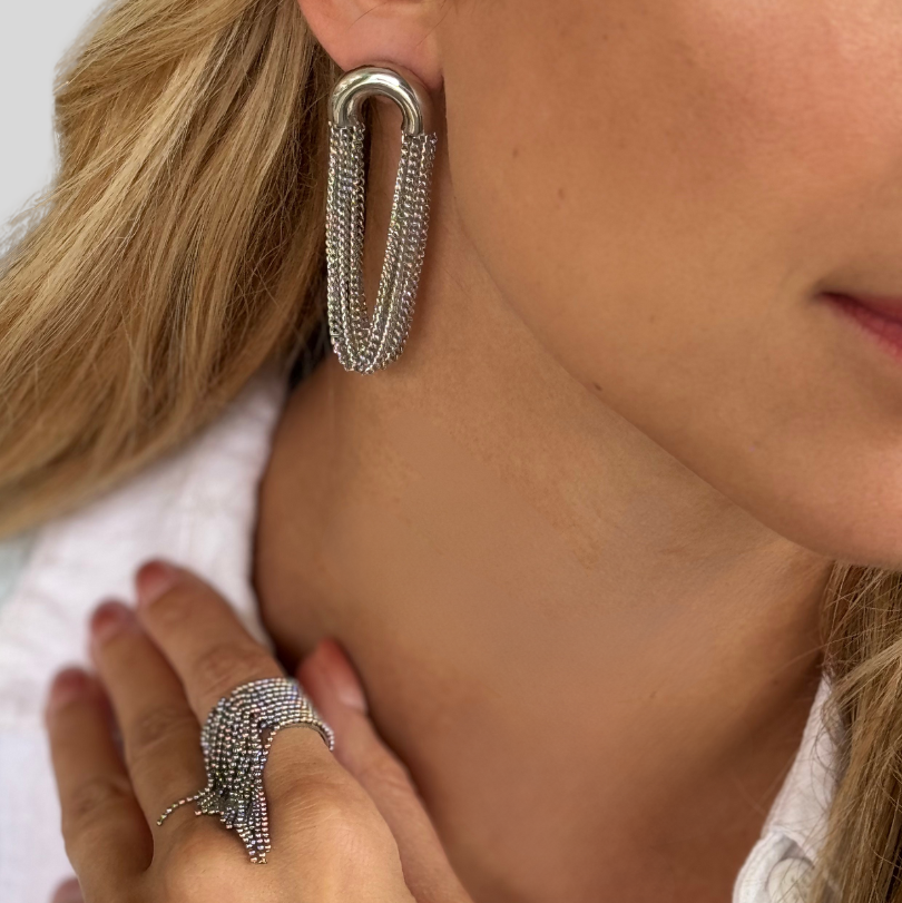 Close-up of a woman wearing silver tassel chain earrings and a ring.