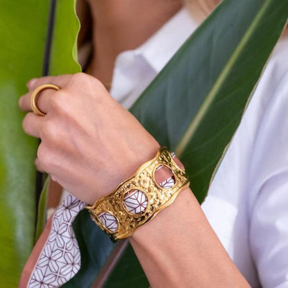 Gold bracelet on a wrist with a white shirt and green leaves in the background